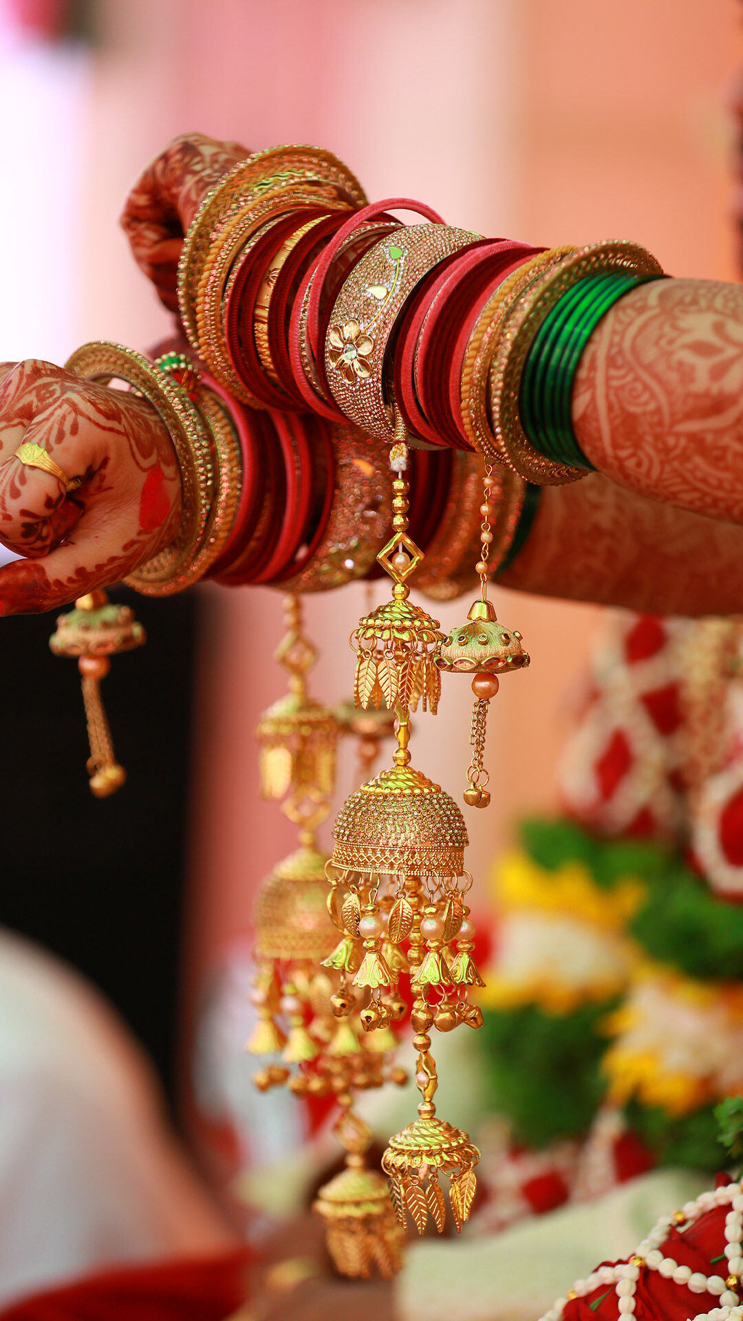 Close-up of bride’s hands adorned with red and green bangles, gold kaleere, and mehndi designs during a traditional Punjabi wedding ceremony